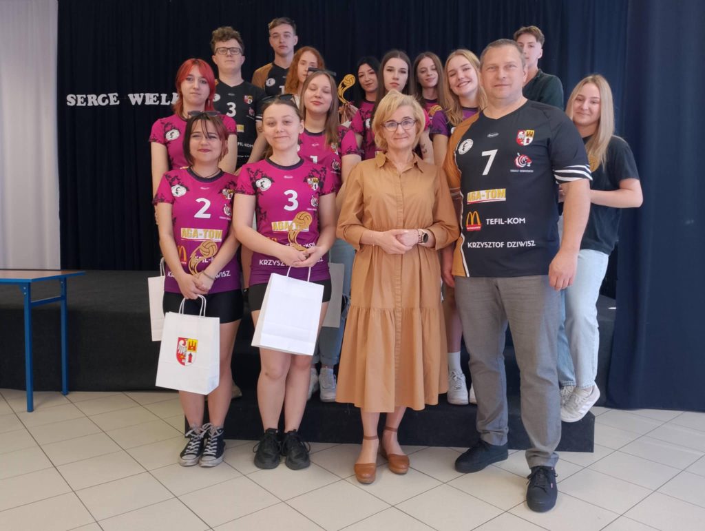 Grupa uczniów w strojach sportowych wraz z panią dyrektor i trenerem, w rekach trzymają puchary i dyplomy.
